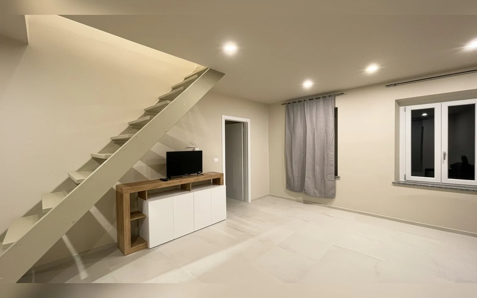 Zona giorno ampia con scala interna e mobile TV in un appartamento COBER IMMOBILIARE a Scarmagno